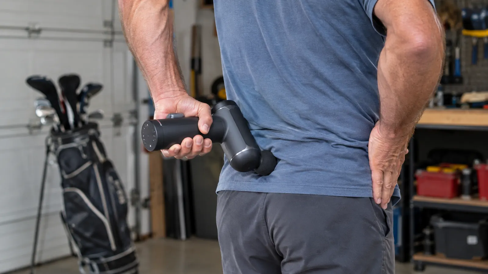 Hands holding a massage gun against a lower back in a garage